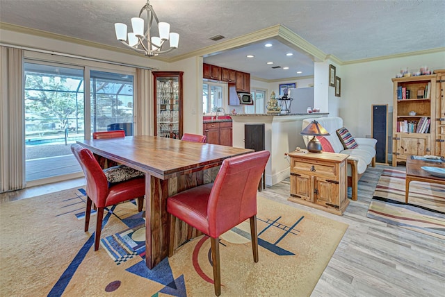 dining room with sink, a chandelier, a textured ceiling, light wood-type flooring, and ornamental molding