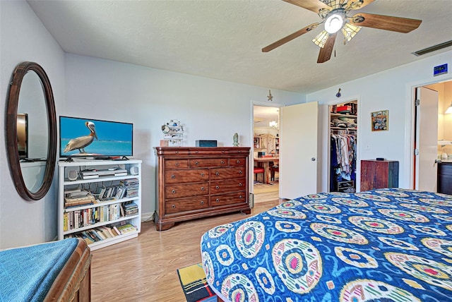 bedroom with a spacious closet, ensuite bathroom, a textured ceiling, and light wood-type flooring