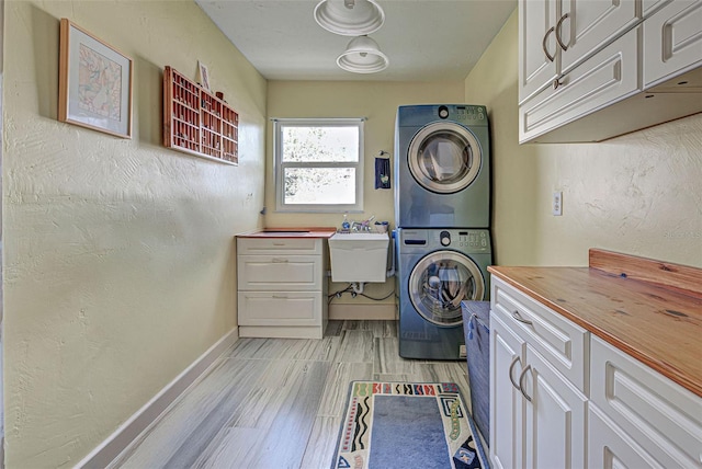 laundry area featuring cabinets, sink, light hardwood / wood-style flooring, and stacked washer and clothes dryer