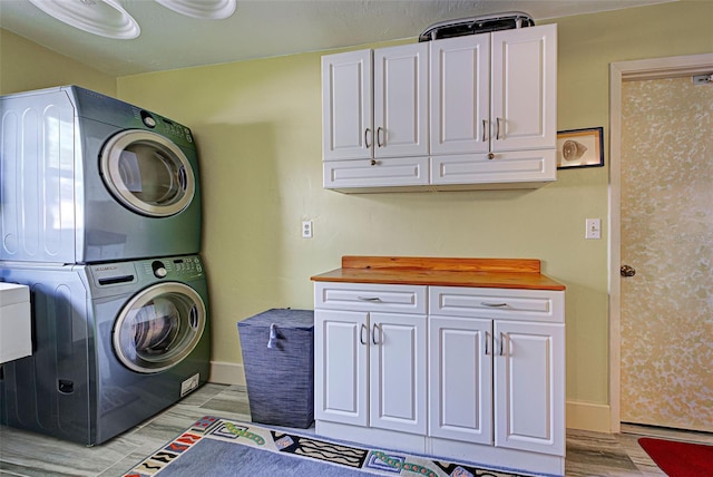 laundry area featuring cabinets, stacked washing maching and dryer, and light hardwood / wood-style floors