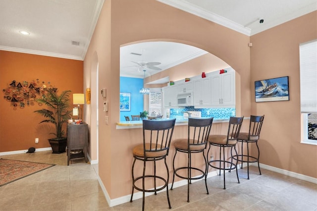 bar with white cabinetry, crown molding, light tile patterned floors, ceiling fan, and decorative backsplash