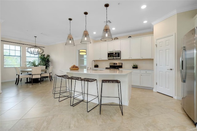 kitchen with crown molding, decorative light fixtures, stainless steel appliances, and an island with sink