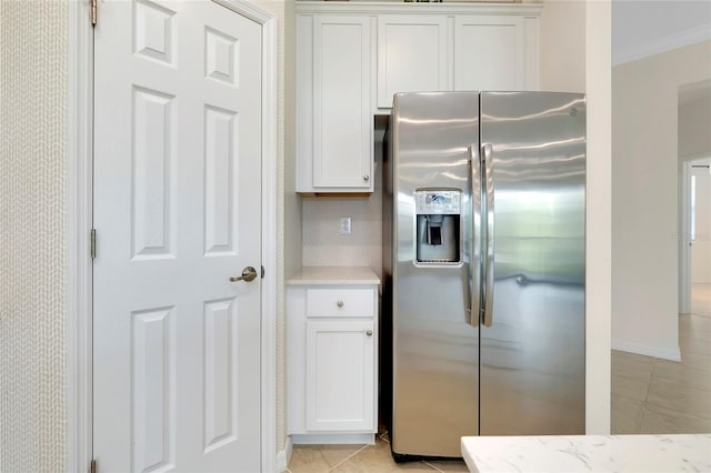 kitchen with light tile patterned floors, crown molding, stainless steel fridge, white cabinetry, and light stone counters