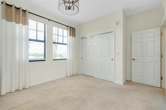 unfurnished bedroom with light colored carpet, a notable chandelier, and a closet