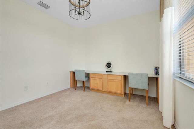 carpeted home office with built in desk and a chandelier