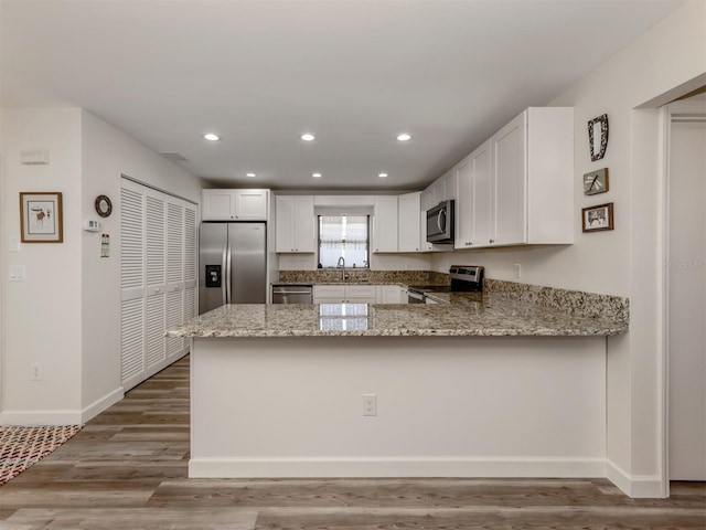 kitchen with white cabinetry, sink, light stone counters, kitchen peninsula, and stainless steel appliances