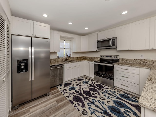 kitchen with sink, white cabinets, stainless steel appliances, light stone countertops, and light hardwood / wood-style flooring