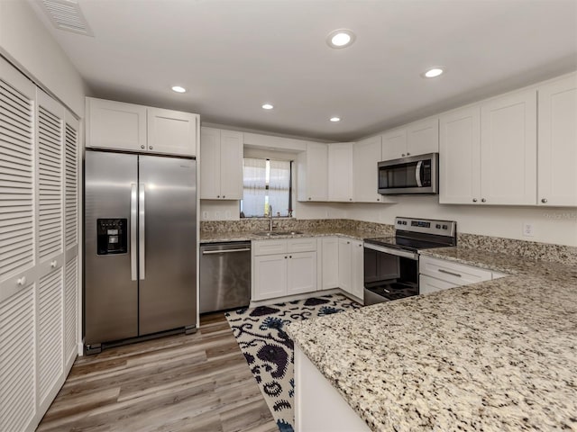 kitchen featuring sink, light stone counters, appliances with stainless steel finishes, light hardwood / wood-style floors, and white cabinets