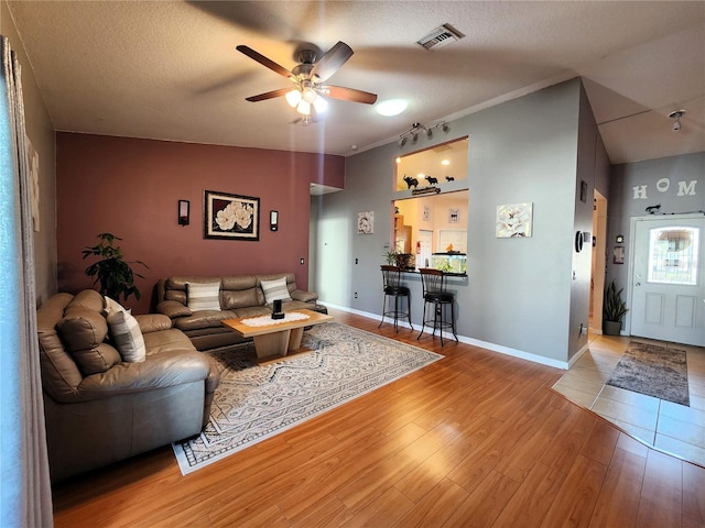 living room featuring ceiling fan, vaulted ceiling, a textured ceiling, and light hardwood / wood-style floors