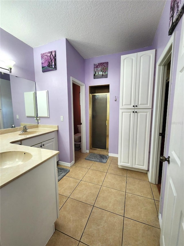 bathroom featuring tile patterned flooring, vanity, walk in shower, toilet, and a textured ceiling