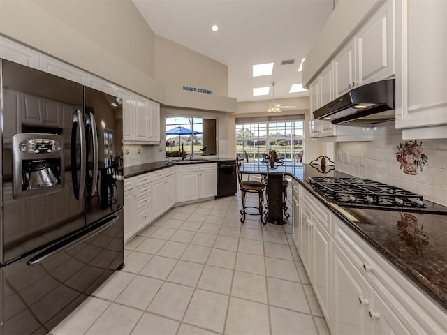 kitchen with white cabinets, backsplash, dark stone counters, light tile patterned floors, and black appliances