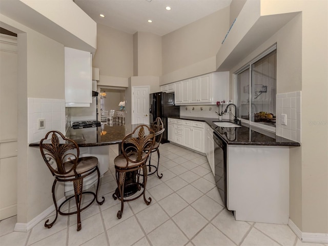 kitchen featuring kitchen peninsula, sink, dark stone countertops, white cabinets, and black appliances