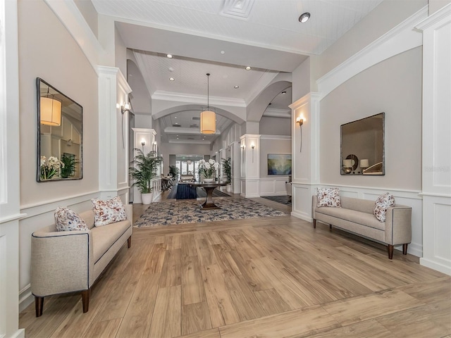 interior space with ornamental molding, a tray ceiling, decorative columns, and light wood-type flooring