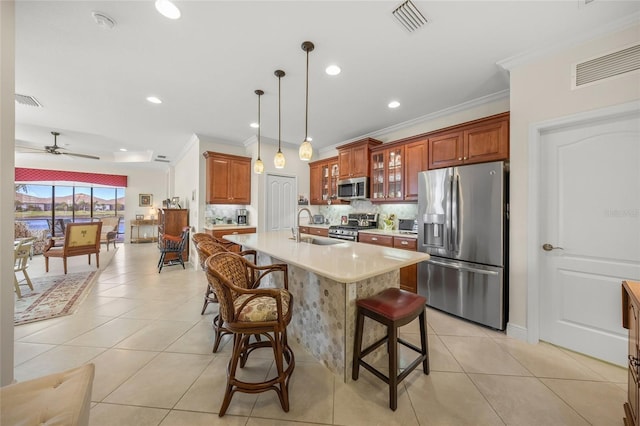 kitchen featuring decorative light fixtures, sink, a kitchen bar, stainless steel appliances, and a center island with sink