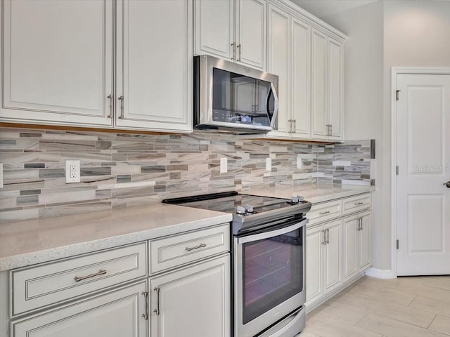 kitchen featuring light stone counters, backsplash, white cabinets, and appliances with stainless steel finishes