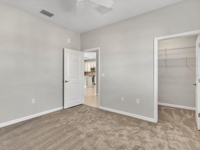 unfurnished bedroom featuring a spacious closet, light colored carpet, ceiling fan, and a closet