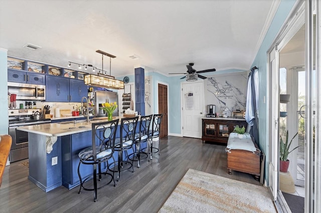 kitchen featuring appliances with stainless steel finishes, a kitchen bar, blue cabinets, dark hardwood / wood-style flooring, and decorative light fixtures