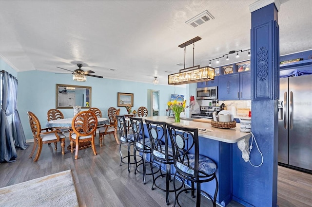 kitchen with blue cabinetry, appliances with stainless steel finishes, dark hardwood / wood-style floors, a kitchen bar, and decorative light fixtures