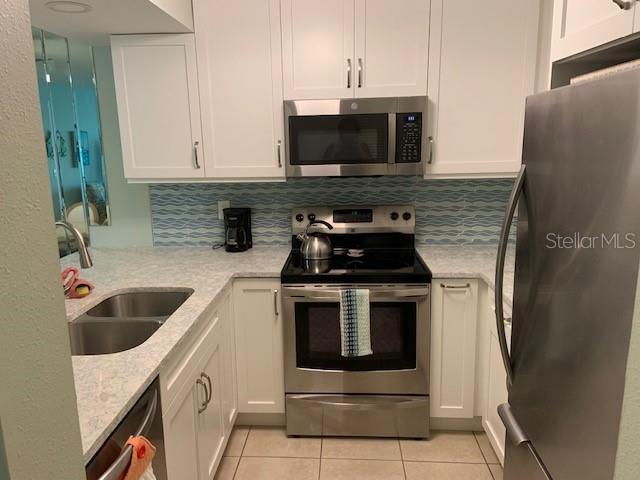 kitchen with light tile patterned floors, appliances with stainless steel finishes, a sink, and white cabinetry