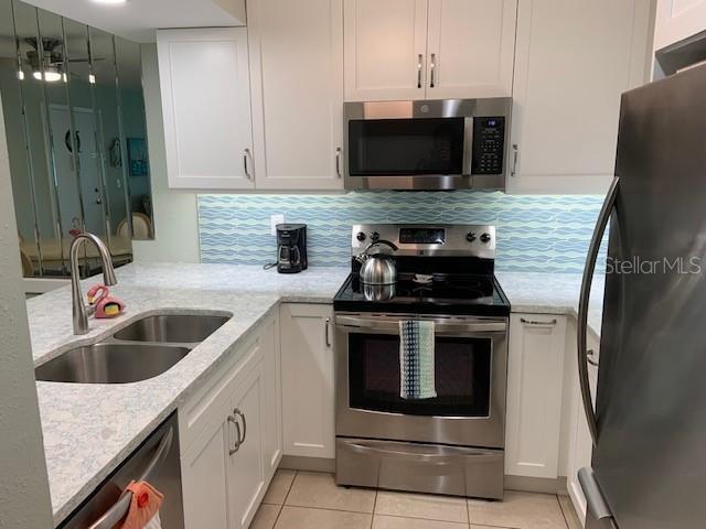 kitchen with light tile patterned floors, white cabinets, appliances with stainless steel finishes, light stone countertops, and a sink