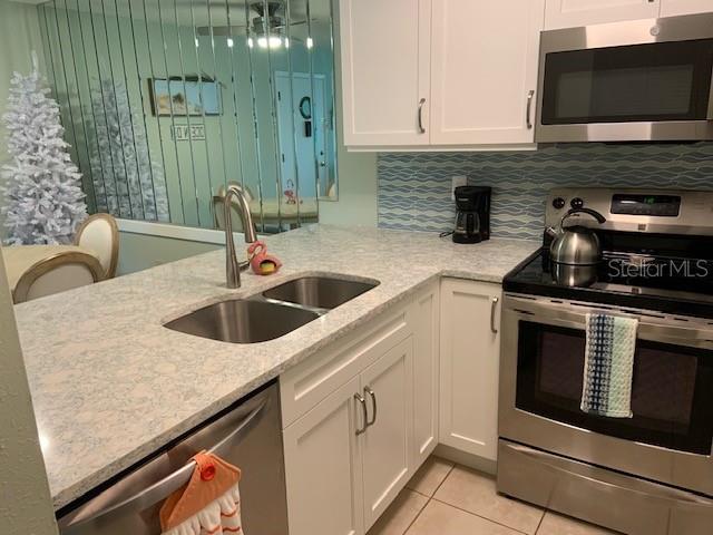 kitchen featuring light tile patterned floors, white cabinets, light stone counters, appliances with stainless steel finishes, and a sink