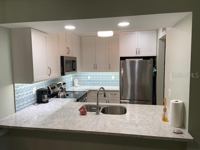 kitchen featuring decorative backsplash, appliances with stainless steel finishes, white cabinetry, a sink, and a peninsula