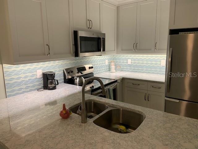 kitchen with light stone counters, appliances with stainless steel finishes, decorative backsplash, and a sink