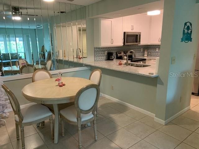 kitchen featuring baseboards, white cabinets, range, decorative backsplash, and stainless steel microwave