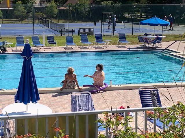 view of swimming pool featuring a tennis court, fence, and a patio