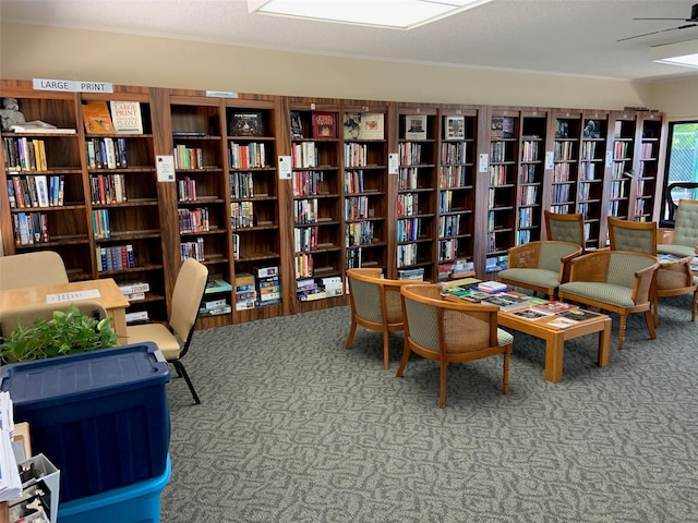 living area featuring bookshelves, carpet flooring, and a ceiling fan