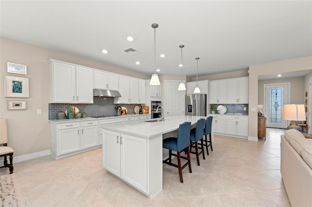 kitchen with white cabinetry, a center island with sink, a kitchen breakfast bar, pendant lighting, and stainless steel appliances