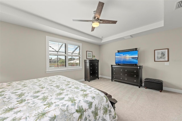 bedroom with a raised ceiling, light colored carpet, and ceiling fan