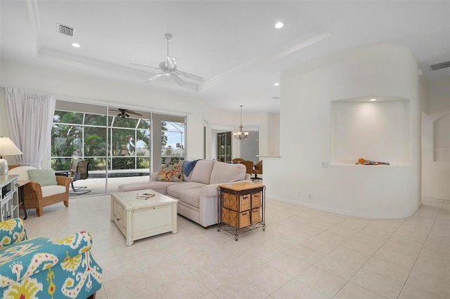 tiled living room with ceiling fan with notable chandelier and a tray ceiling