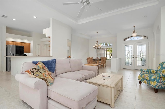 tiled living room featuring crown molding, a tray ceiling, ceiling fan with notable chandelier, and french doors