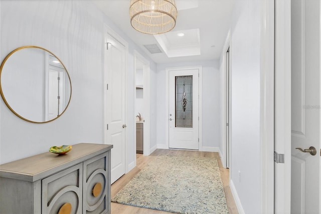 hall with a tray ceiling and light wood-type flooring