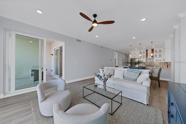 living room featuring hardwood / wood-style flooring, ornamental molding, sink, and ceiling fan