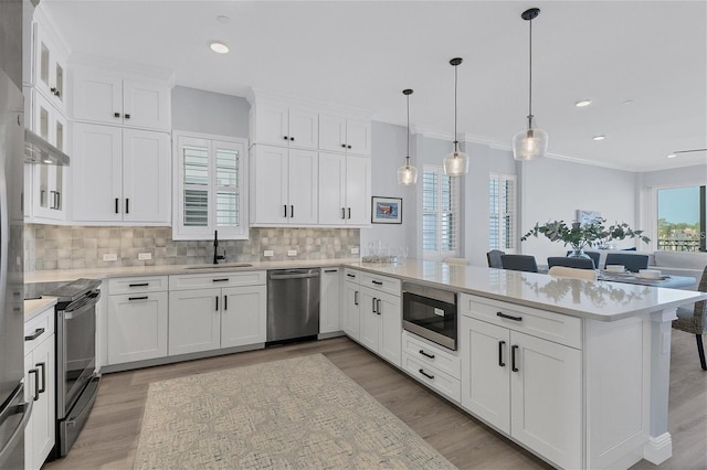 kitchen with appliances with stainless steel finishes, kitchen peninsula, hanging light fixtures, and white cabinets