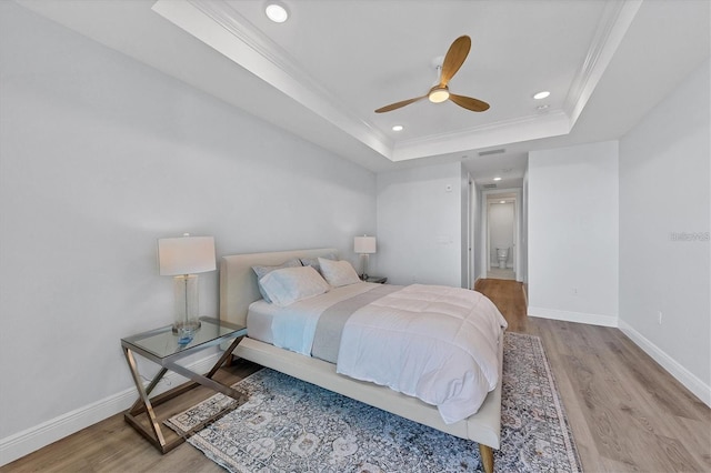 bedroom featuring ornamental molding, light hardwood / wood-style flooring, ceiling fan, and a tray ceiling