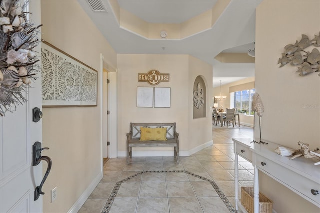 entryway with light tile patterned floors, a raised ceiling, and a chandelier