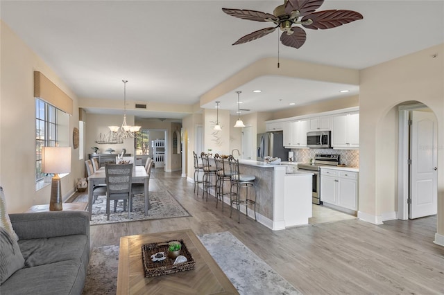 living room featuring ceiling fan with notable chandelier and light wood-type flooring