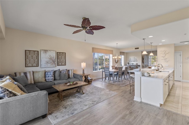 living room featuring sink, ceiling fan with notable chandelier, and light hardwood / wood-style floors