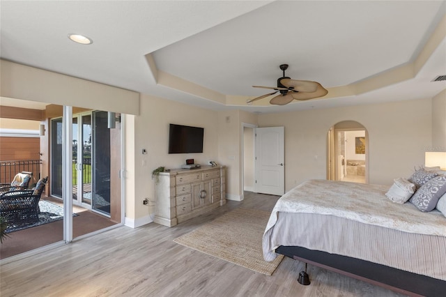 bedroom with ensuite bath, access to outside, a raised ceiling, hardwood / wood-style flooring, and ceiling fan