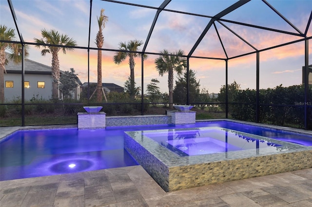 pool at dusk featuring an in ground hot tub, a lanai, and a patio area