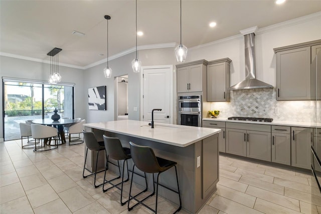 kitchen featuring pendant lighting, wall chimney range hood, sink, a kitchen island with sink, and stainless steel appliances