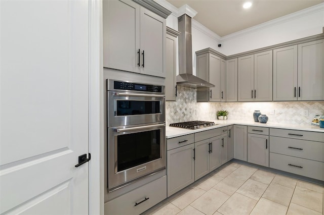 kitchen with gray cabinetry, tasteful backsplash, appliances with stainless steel finishes, ornamental molding, and wall chimney range hood