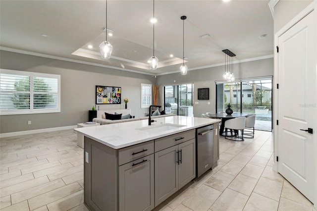 kitchen with sink, gray cabinetry, a raised ceiling, light stone countertops, and a kitchen island with sink