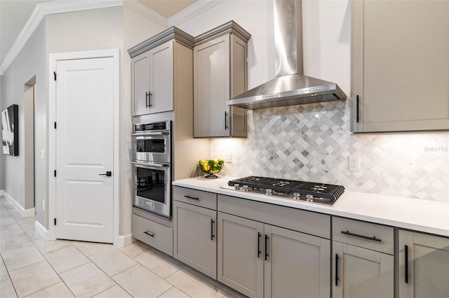 kitchen featuring light tile patterned floors, crown molding, appliances with stainless steel finishes, tasteful backsplash, and wall chimney exhaust hood