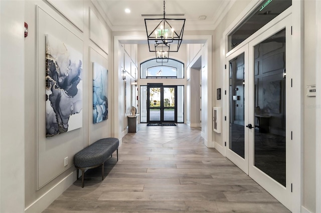 interior space with ornamental molding, light hardwood / wood-style floors, an inviting chandelier, and french doors