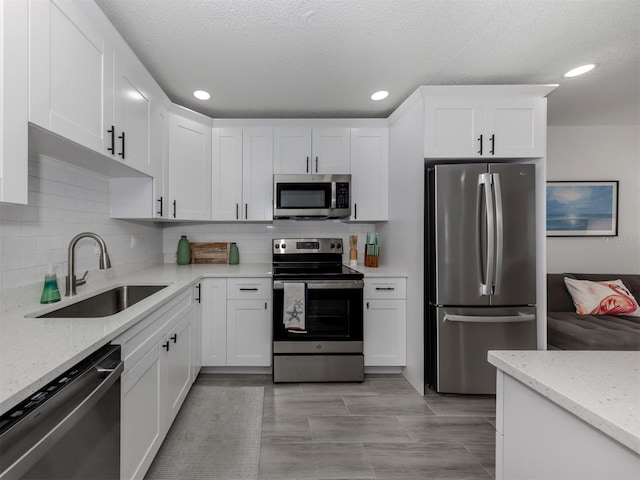 kitchen with stainless steel appliances, white cabinetry, sink, and light stone counters