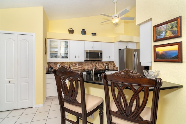 kitchen featuring lofted ceiling, appliances with stainless steel finishes, tasteful backsplash, white cabinets, and light tile patterned flooring